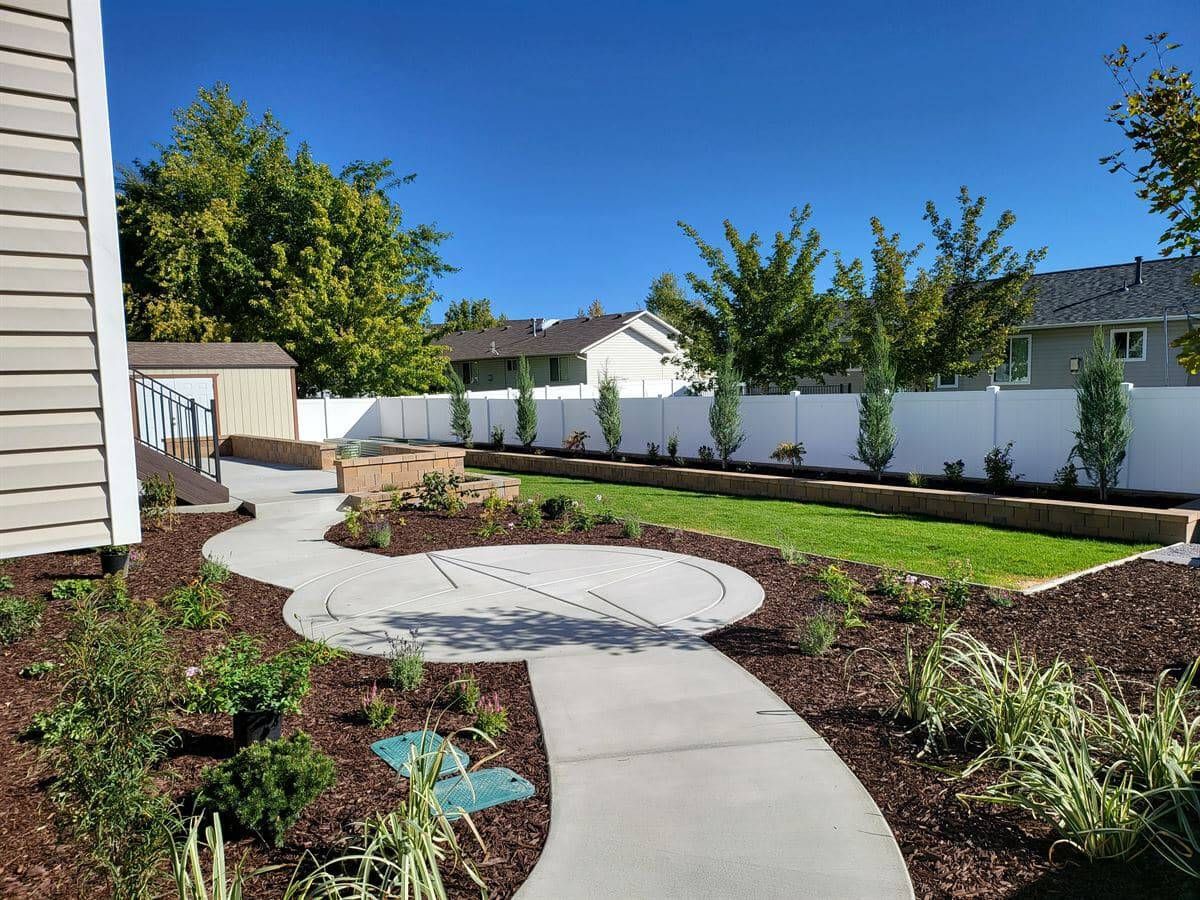 Concrete walkway in West Jordan leading to backyard patio with planting beds along the side.