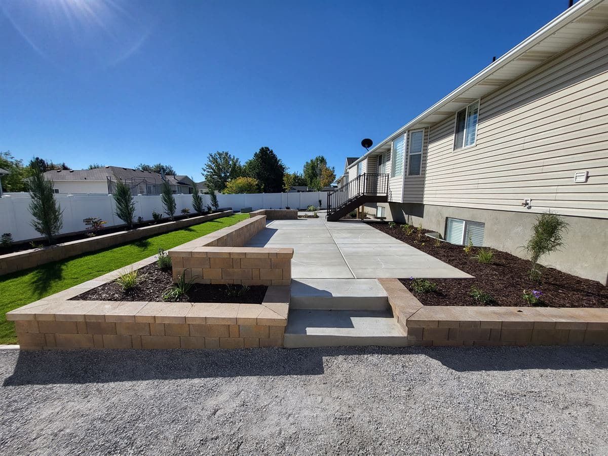 Completed backyard concrete patio with tiered block retaining walls and lawn